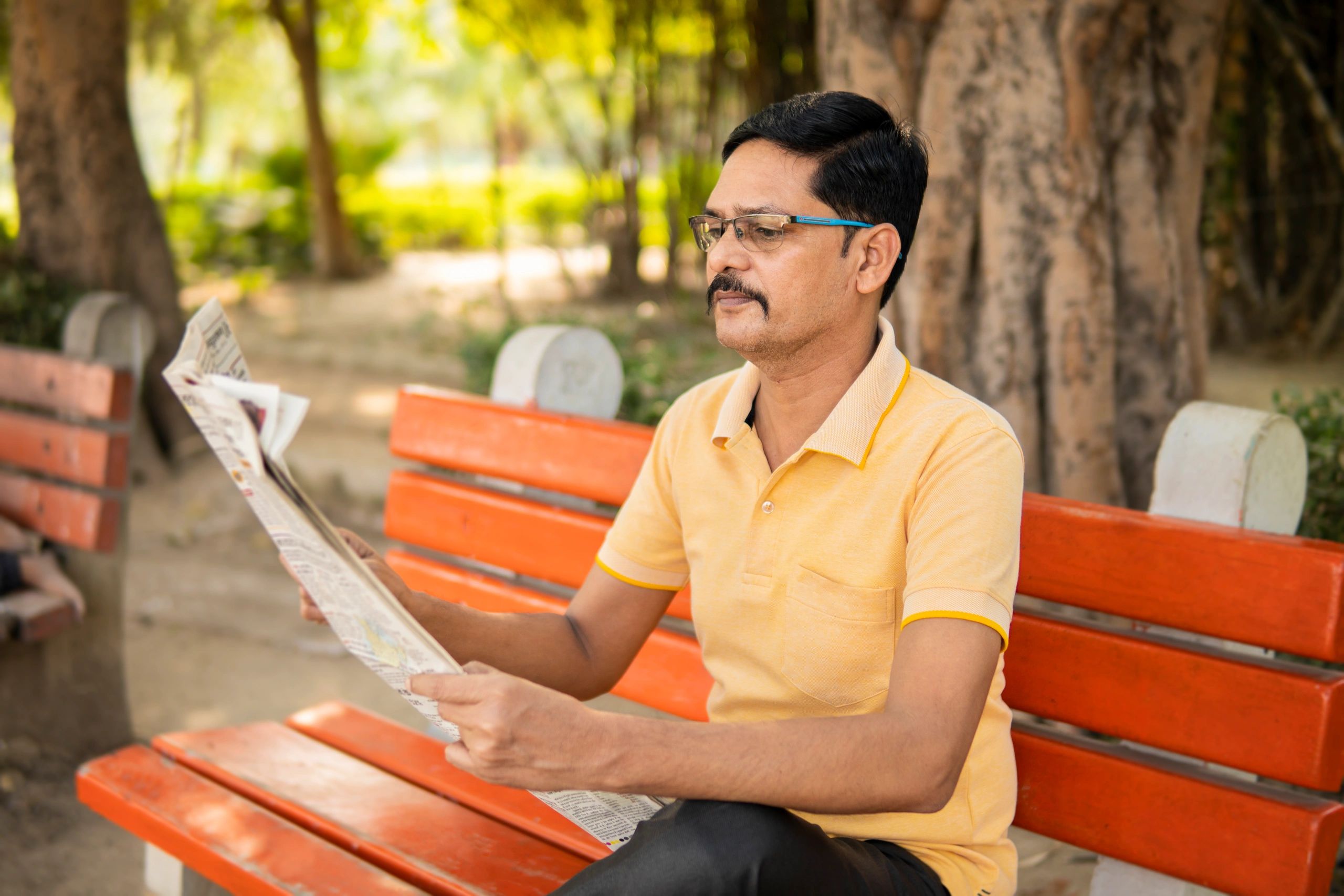 Indian man reading a newspaper in a park